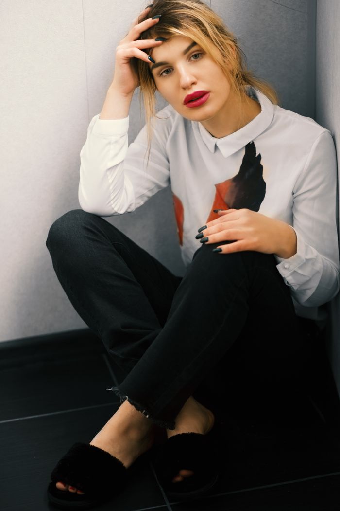 why-choose-us Portrait of a fashionable young woman in a relaxed sitting pose, wearing casual attire and red lipstick.